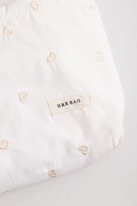 Close-up of heart embroidery on striped fabric and brand label for makeup bag