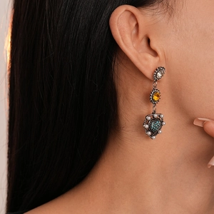 Dettaglio di orecchini vintage a cuore con cristalli blu e perle indossati dal modello