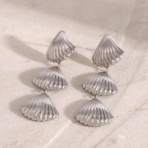 Polished silver stainless steel triple shell drop earrings on a stone surface