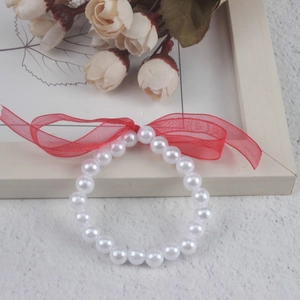 Macro shot of white imitation pearl bracelet with a red decorative ribbon detail