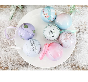 Spherical tin candy boxes with floral patterns and ribbons on a snowy wooden background