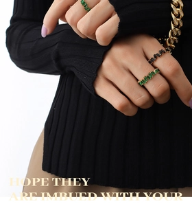 Detail of model wearing emerald and black rectangle cut rings with gold chain bracelet