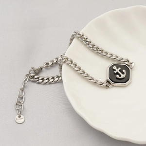 Close-up of stainless steel Cuban chain bracelet featuring a black anchor octagonal charm