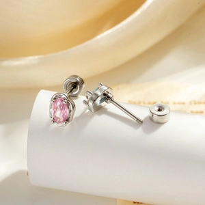 Minimalist silver stud earrings with pink oval zircon on a white display stand