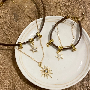 Flat lay of sun and star necklaces with brown cords on a white ceramic plate