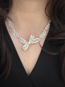 Détail du collier noeud argenté avec pendentif perle et texture dentelle sur peau