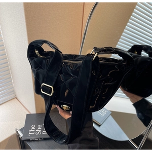 Detail of glossy quilted black crossbody bag with gold hardware and wide shoulder strap