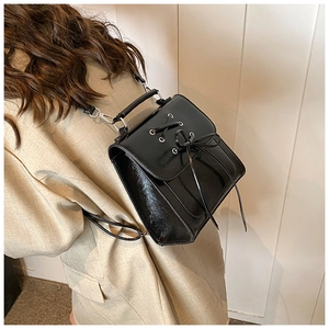 Side view of a black shiny mini backpack with bow detail worn by a model in casual blazer