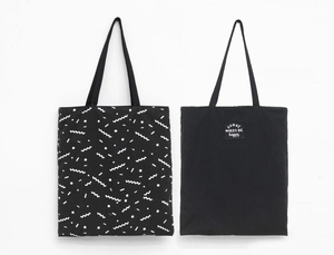 Detail view of two black canvas tote bags with wave pattern and embroidered slogan patch