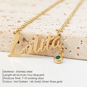 Macro detail of custom 14k gold plated name necklace with green gemstone on stone background