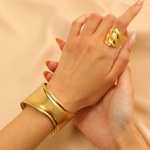 Detailed close-up of a gold-plated chunky spiral ring and smooth wide cuff bracelet