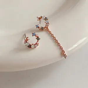 Asymmetric rose gold earrings with pink and blue stones on white ceramic dish