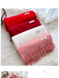 Detail of neatly stacked solid color cashmere-feel scarves with soft fringe and fabric labels