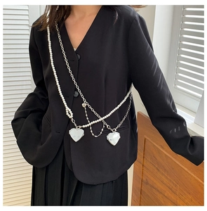 Detail of layered silver chain and pearl body jewelry with two heart-shaped pendants