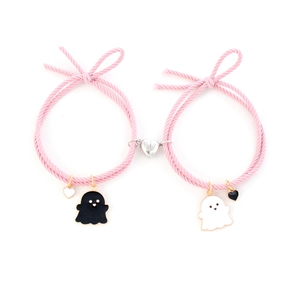 Close-up of pink woven couple bracelets with black and white ghost charms and magnetic heart