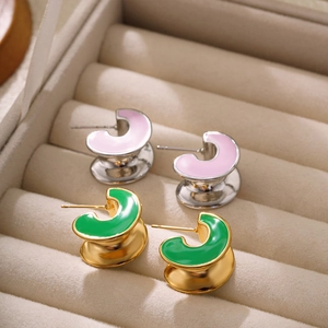 Detailed macro view of C-shaped enamel earrings in pink and green on a velvet box