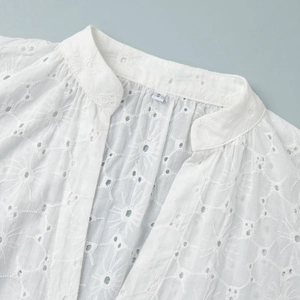 Detail of white cotton lace dress featuring sunflower embroidery and ruffled stand collar