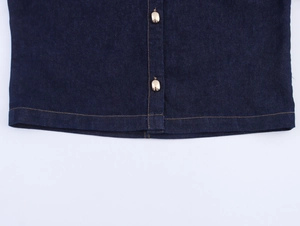 Detailansicht von dunkelblauem Denim-Saum mit gelben Ziernähten und Goldknopf