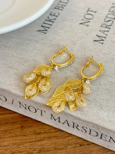 Macro shot of gold leaf earrings with cubic zirconia on a vintage linen book background
