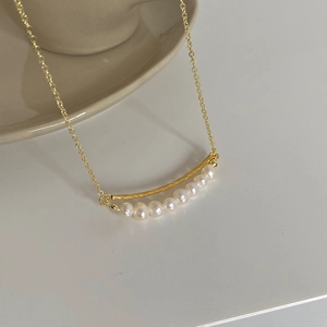 Close-up of gold twisted bar necklace with seven white freshwater pearls on ceramic edge