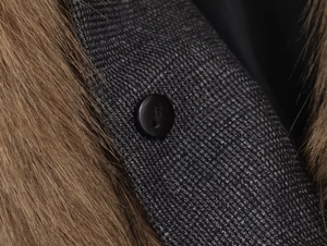 Dettaglio del tessuto tweed grigio con collo in pelliccia sintetica marrone e bottone