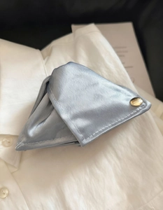Détail d'une pince à cheveux en satin bleu clair avec bouton doré sur tissu de coton blanc