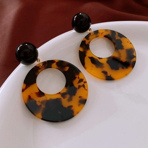 Detail of leopard print resin hoop earrings on a ceramic dish with fabric background