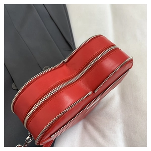 Detail of red heart-shaped leather bag showing silver double zippers and premium texture