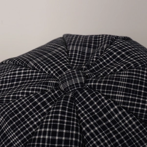 Close-up of black and white plaid newsboy cap showing top button and stitched panels