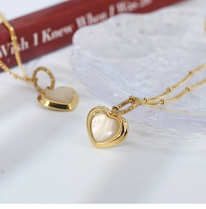 Close-up of gold heart necklace with white mother of pearl inlay on frosted glass tray