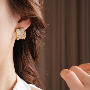 Détail d'une boucle d'oreille C dorée avec incrustation florale blanche sur l'oreille