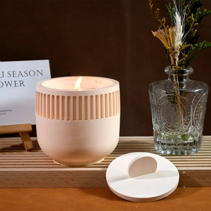 Detail of a lit candle in a pink striped ceramic jar with a lid on a wooden stand