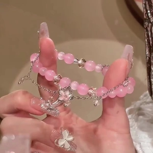 Détail de bracelets perlés avec pierres oeil-de-chat roses, charms papillon et fleurs