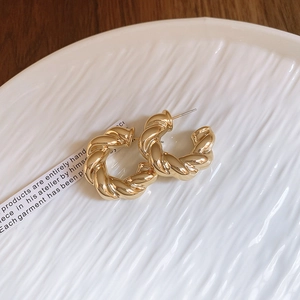 Detailed view of golden twisted C-shape hoop earrings on a textured ceramic plate