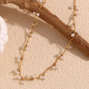Close-up of wavy gold necklace with white pearls draped on a natural wooden branch