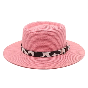 Pink flat top straw sun hat with cow print band and silver buckle on white background