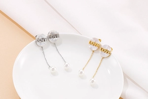 Detail of gold and silver long earrings featuring shell LOVE charms and pearl drops
