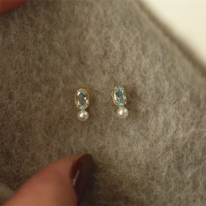 Macro detail of S925 silver gold-plated stud with blue topaz and round white pearl