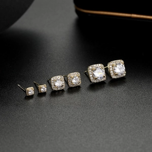 Close-up of three pairs of golden square zircon stud earrings set in different sizes