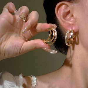 Detailed view of triple-layered gold hoop earrings with zircon pavé and a butterfly ring