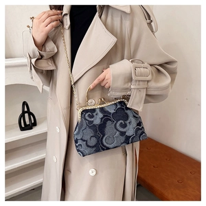 Detail view of denim cloud pattern crossbody bag with gold frame on beige coat