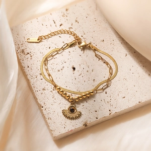 Double-layered gold stainless steel bracelet with sun pendant on stone and silk background