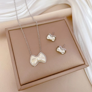 Titanium steel jewelry set with pearl bow necklace and earrings on white silk fabric