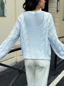 Rear view of a light blue cable knit cardigan sweater with a relaxed fit on model
