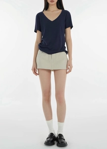 Full view of women's navy V-neck t-shirt styled with beige mini skirt and black loafers