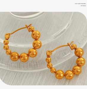 Macro detail of gold beaded hoop earrings with gradient pearls on textured white fabric