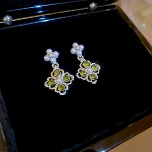 Macro shot of clover earrings with green zircons and pearls on black velvet