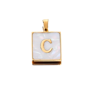Macro detail of square stainless steel pendant featuring a gold letter C on white shell