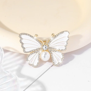 Macro detail of butterfly brooch featuring white enamel wings and faux pearl body