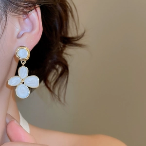 Détail de boucles d'oreilles fleur dorées avec émail blanc portées par un mannequin
